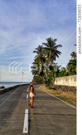 woman walking alone at the empty tropical road with lots of palm trees in Cebu Island in Philippines 71850055