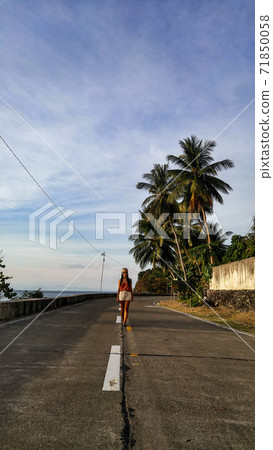 woman walking alone at the empty tropical road with lots of palm trees in Cebu Island in Philippines 71850058