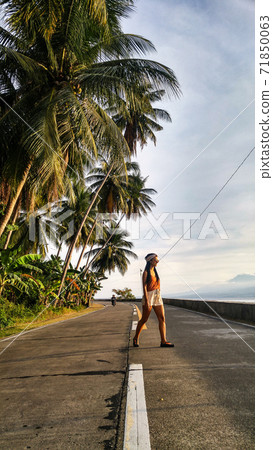 woman walking alone at the empty tropical road with lots of palm trees in Cebu Island in Philippines 71850063