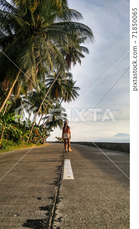 woman walking alone at the empty tropical road with lots of palm trees in Cebu Island in Philippines 71850065
