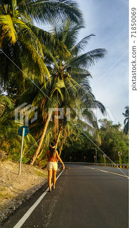 woman walking alone at the empty tropical road with lots of palm trees in Cebu Island in Philippines 71850069
