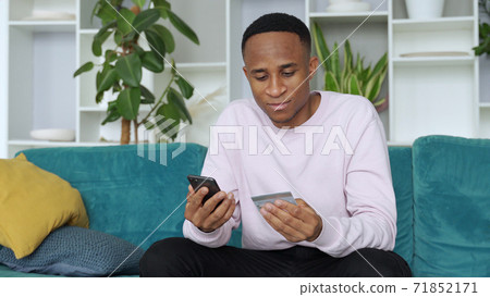 Online payment. African-american man holding credit card and using smartphone for shopping in internet at home 71852171