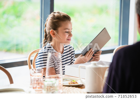 A portrait of a pretty girl sitting at a table with a tablet. A portrait of a pretty girl sitting at a table with a tablet. 71852653