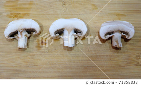 Flay lay of 3 slices of cut white button mushrooms, arranged side by side on a wooden cutting board surface. 71858838