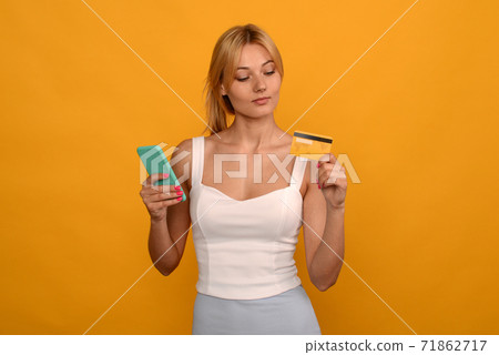 Lady buying online with a credit card and smart phone on yellow background Lady buying online with a credit card and smart phone on yellow background 71862717