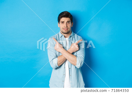 Portrait of nervous guy pointing fingers sideways, looking indecisive and asking for help with choice, showing left and right promo offers, standing against blue background Portrait of nervous guy pointing fingers sideways, looking indecisive and asking for help with choice, showing left and right promo offers, standing against blue background 71864350