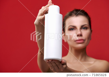 Beautiful woman shows a bottle of shampoo on a red background. Beautiful woman shows a bottle of shampoo on a red background. 71865828
