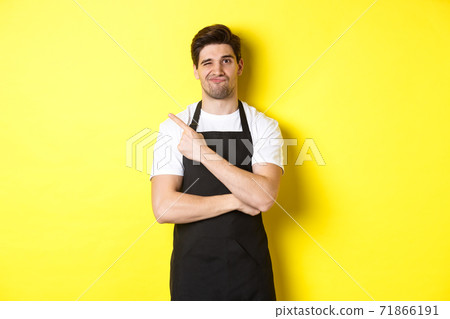 Displeased barista in black apron pointing finger at upper left corner, grimacing skeptical, dislike something, standing against yellow background Displeased barista in black apron pointing finger at upper left corner, grimacing skeptical, dislike something, standing against yellow background 71866191