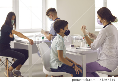 Boy waiting for his shot and looking at the needle as the nurse gets the vaccine ready Boy waiting for his shot and looking at the needle as the nurse gets the vaccine ready 71867145