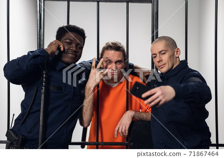 A prisoner with tattoos on his face takes a selfie with his fellow prison guards on a smartphone. 71867464
