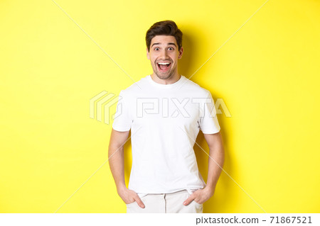 Man looking surprised, smiling amazed and looking at announcement, standing near copy space, yellow background 71867521