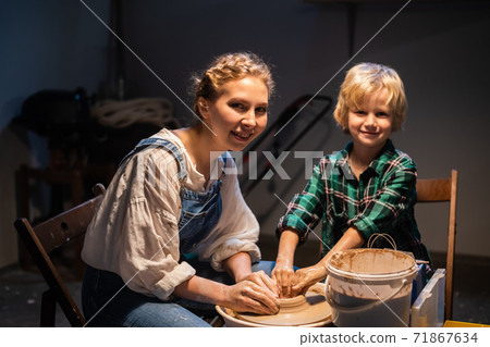 a young mother and her young son pose for a photo in a pottery workshop, modeling dishes from clay. a young mother and her young son pose for a photo in a pottery workshop, modeling dishes from clay. 71867634