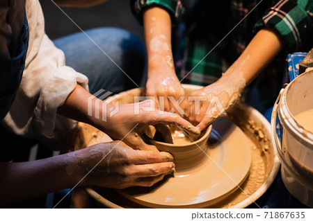 the process of modeling clay dishes on a potter's wheel, the hands of a young girl and a child. the process of modeling clay dishes on a potter's wheel, the hands of a young girl and a child. 71867635