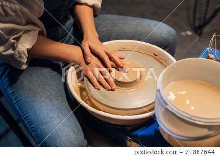 beautiful hands of a young potter's girl in the process of modeling a pot in the workshop. beautiful hands of a young potter's girl in the process of modeling a pot in the workshop. 71867644