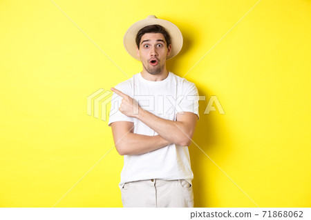 Concept of tourism and lifestyle. Surprised handsome man tourist pointing finger left, looking impressed about promo offer, yellow background Concept of tourism and lifestyle. Surprised handsome man tourist pointing finger left, looking impressed about promo offer, yellow background 71868062