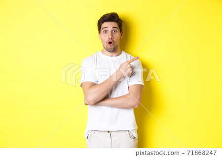 Portrait of surprised handsome man pointing finger right, gasping amazed, standing over yellow background Portrait of surprised handsome man pointing finger right, gasping amazed, standing over yellow background 71868247