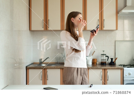 Young woman doing make up in kitchen and looking in mirror. Hurrying to work 71868874