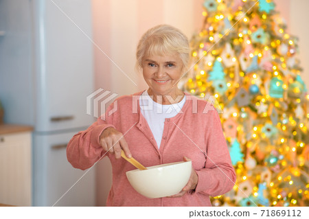 Smiling grey-haired woman stirring something in a bowl Smiling grey-haired woman stirring something in a bowl 71869112