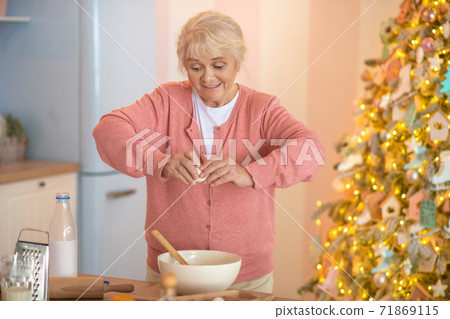 Smiling grey-haired woman breaking eggs into the bowl 71869115