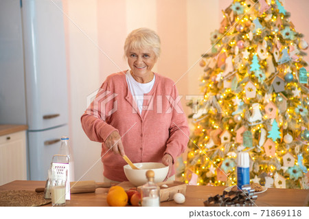 Smiling grey-haired woman cooking something in the kitchen and looking happy 71869118
