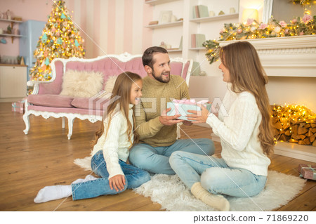 Young family sitting on the floor and exchanging christmas gifts Young family sitting on the floor and exchanging christmas gifts 71869220