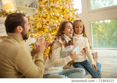 Young family sitting near christmas tree and feeling happy Young family sitting near christmas tree and feeling happy 71869225