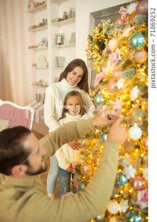 Dad putting balls on christmas tree while his wife and daughter watching him Dad putting balls on christmas tree while his wife and daughter watching him 71869252