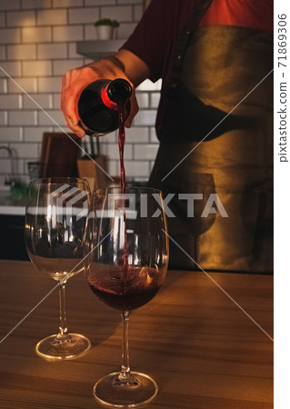 A man pours red wine into a glass A man pours red wine into a glass 71869306