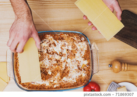 Man's hands making lasagna in glass tray, top view. Man's hands making lasagna in glass tray, top view. 71869307