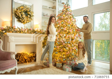 Cute young family decorating christmas tree at home Cute young family decorating christmas tree at home 71869755