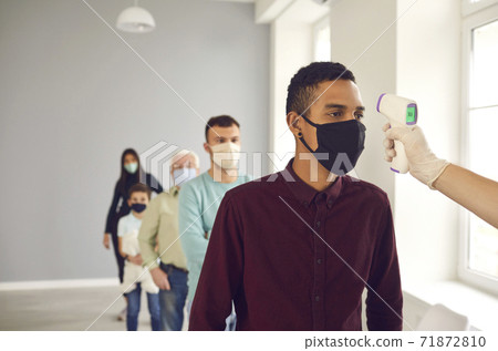 Man, standing in line in public place, gets his body temperature measured with infrared thermometer Man, standing in line in public place, gets his body temperature measured with infrared thermometer 71872810