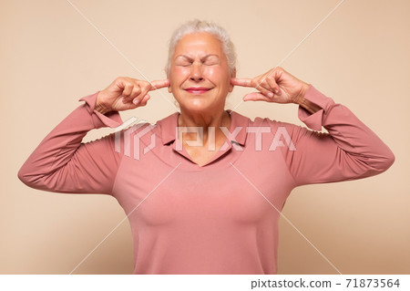 Angry annoyed senior woman plugging her ears to avoid loud noise 71873564