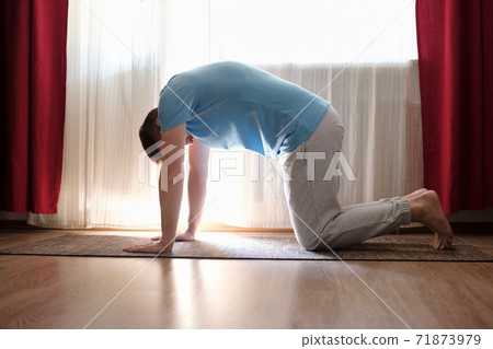 man practices yoga asana marjariasana or cow pose at home. man practices yoga asana marjariasana or cow pose at home. 71873979