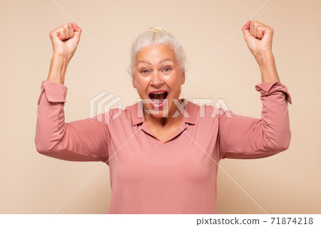 Happy middle aged caucasian woman raising fists in winning gesture and celebrating success 71874218