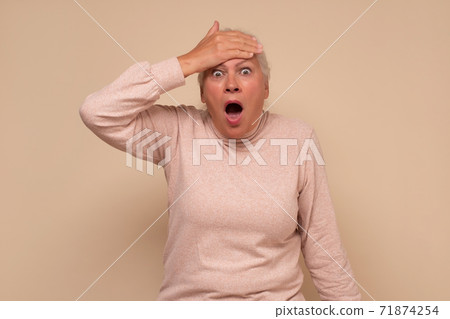 Shocked senior woman , keeping hands up looking with great surprisment and amazement into camera 71874254