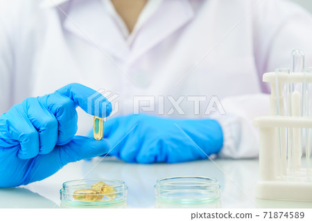 Scientist hands putting in nitrile blue latex gloves  holding Omega 3 capsule in labcoat 71874589