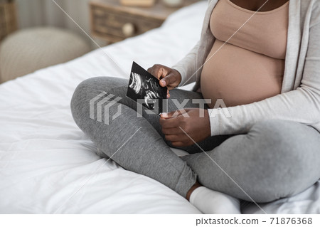 Black Pregnant Woman Looking At Ultrasound Image Of Her Baby On Bed Black Pregnant Woman Looking At Ultrasound Image Of Her Baby On Bed 71876368