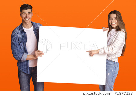 Excited millennial couple in love showing poster with empty space for text, woman pointing on it 71877158