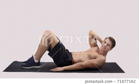 Smiling millennial guy with naked chest doing abs exercises on sports mat over light studio background, panorama 71877162