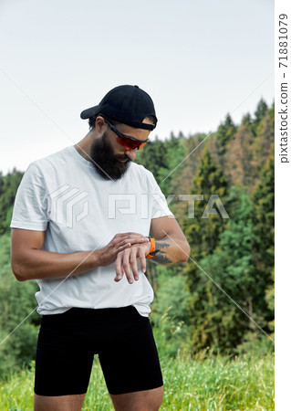 Healthy smart lifestyle concept. Muscular athlete doing great exercising outside in sunny park. Young handsome man in sportswear checking sport tracker watch. 71881079