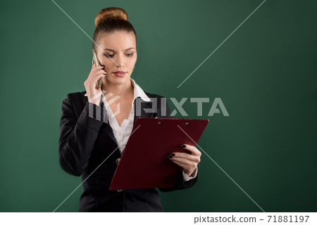 Pretty businesswoman with clipboard talks on phone green background 71881197