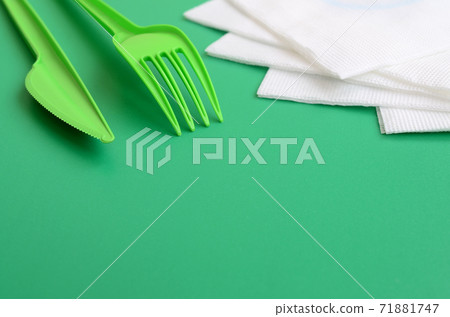 Disposable plastic cutlery green. Plastic fork and knife lie on a green background surface next to napkins Disposable plastic cutlery green. Plastic fork and knife lie on a green background surface next to napkins 71881747