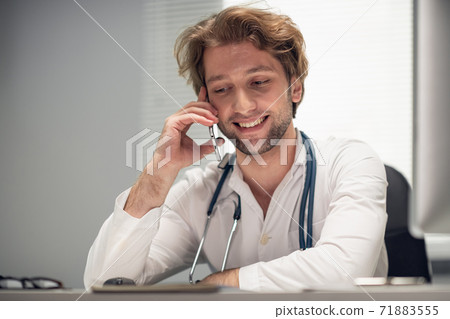 Smiling, handsome doctor on the phone in his office Smiling, handsome doctor on the phone in his office 71883555