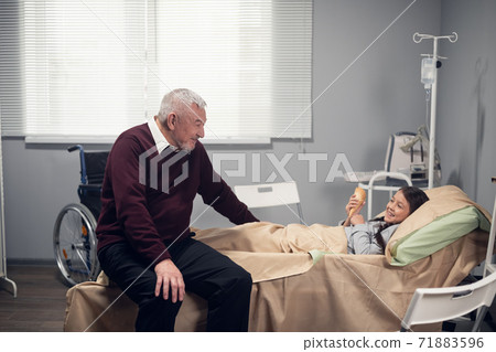 medicine, support, family health care and people concept. Happy senior man visiting his granddaughter, who is lying in bed at a hospital ward medicine, support, family health care and people concept. Happy senior man visiting his granddaughter, who is lying in bed at a hospital ward 71883596