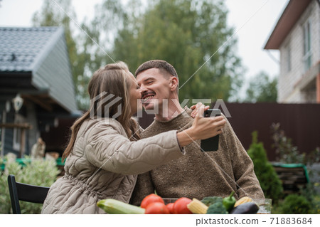 A young couple in love celebrates the purchase of a new country house. Kissing for selfies in the background of the house for social networks. 71883684