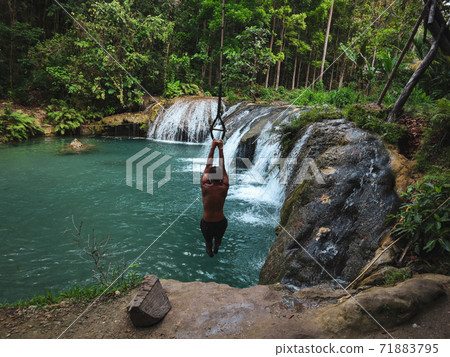 man swinging with the rope at the pool of waterfalls, Cambugahay Falls on Siquijor Island in Philippines man swinging with the rope at the pool of waterfalls, Cambugahay Falls on Siquijor Island in Philippines 71883795