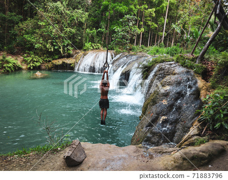 man swinging with the rope at the pool of waterfalls, Cambugahay Falls on Siquijor Island in Philippines 71883796
