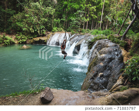man swinging with the rope at the pool of waterfalls, Cambugahay Falls on Siquijor Island in Philippines man swinging with the rope at the pool of waterfalls, Cambugahay Falls on Siquijor Island in Philippines 71883797