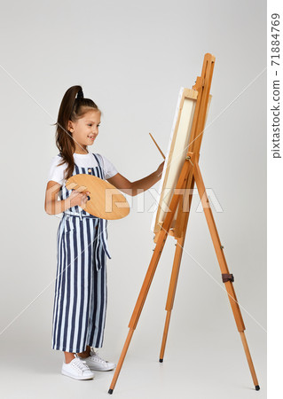 Portrait of beautiful little girl holding a wooden art palette and brush on studio background 71884769