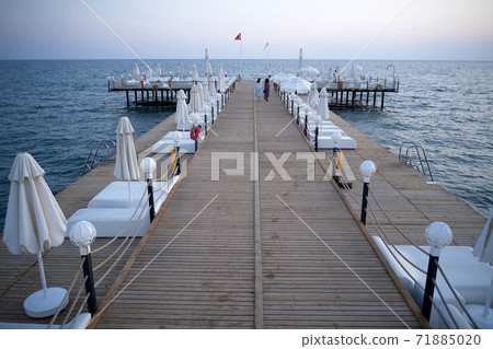Wooden bridge with sunbeds in the sea at sunset. Wooden bridge with sunbeds in the sea at sunset. 71885020